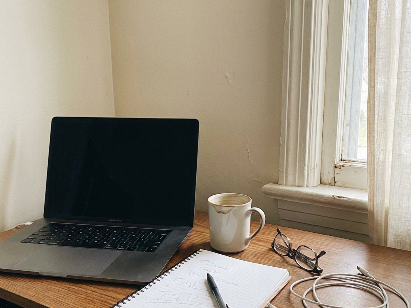 My desk: laptop, notebook and coffee by the window